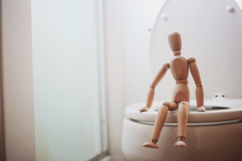 Bild på en träfigur som sitter på en toalettstol